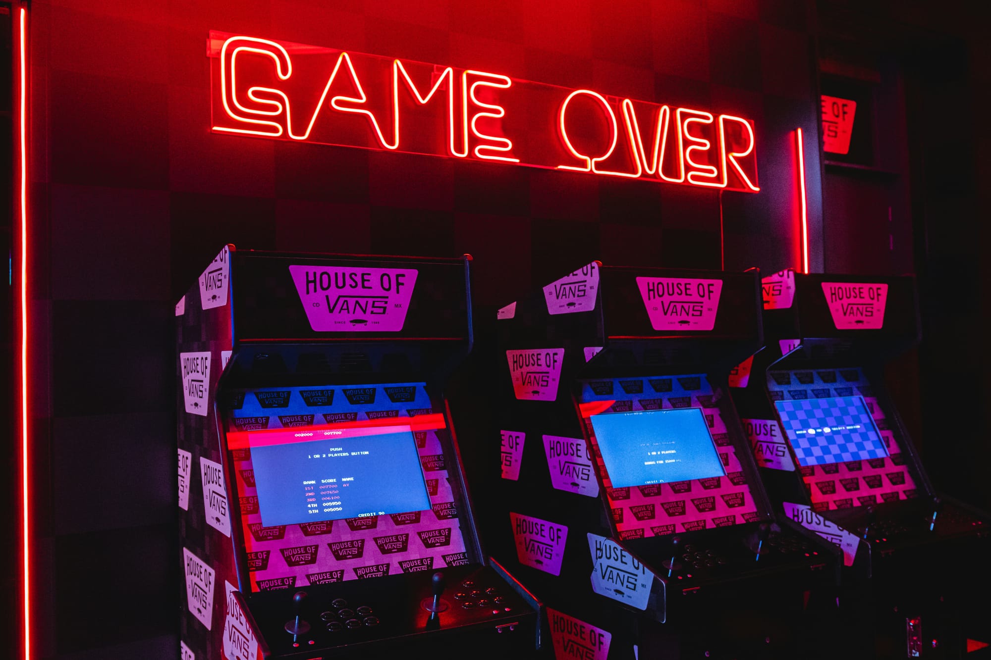 Retro arcade with neon "GAME OVER" sign and classic arcade cabinets bathed in red and purple lighting, evoking nostalgic gaming memories.