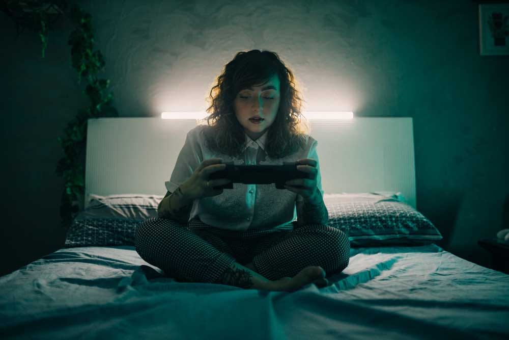 A young lady sitting on a bed with the new ASUS ROG Xbox Ally X in her hands. 