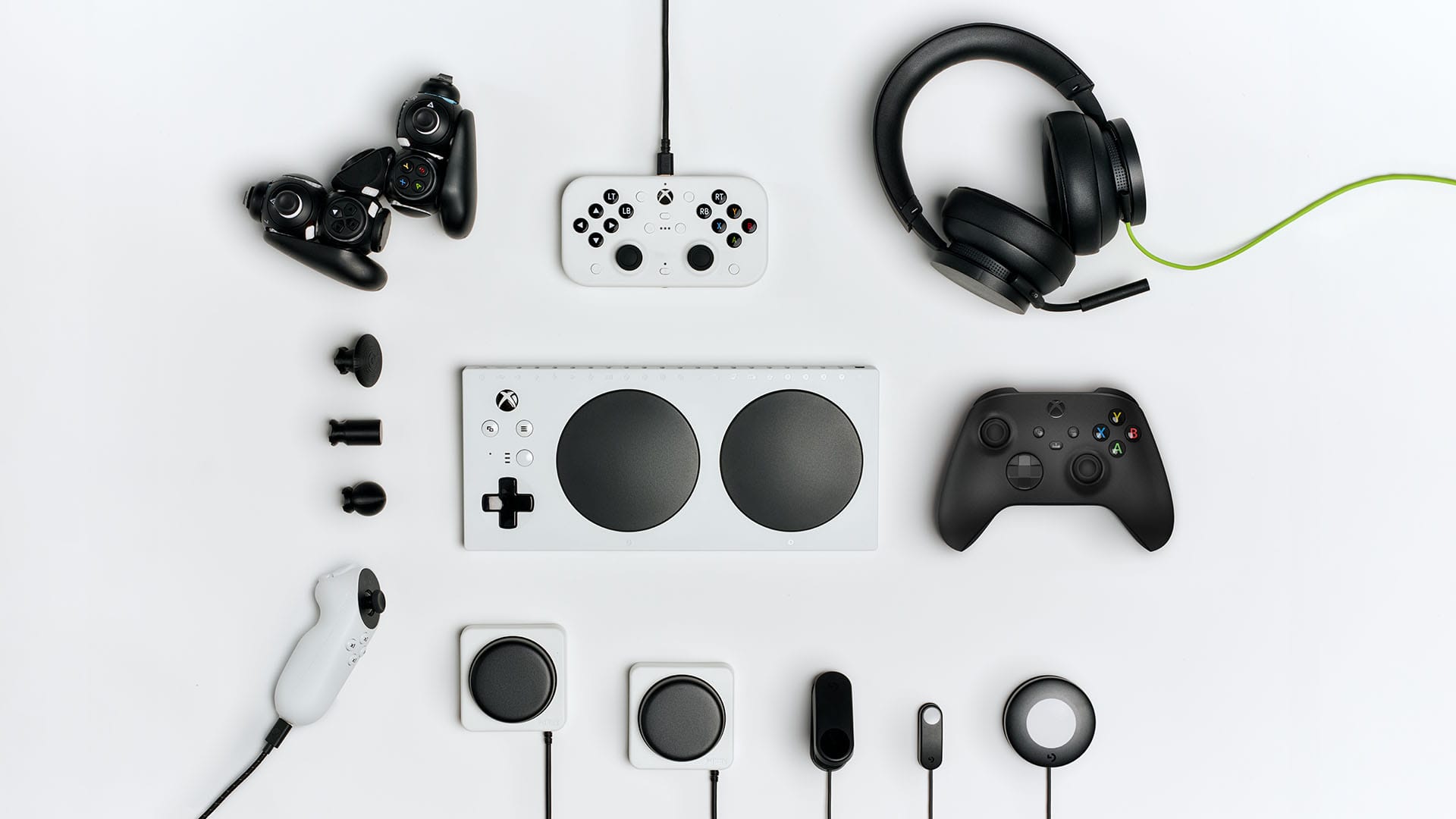 Xbox Adaptive Controller with various accessibility inputs, standard controllers, and gaming headset displayed on white background, showing inclusive gaming options